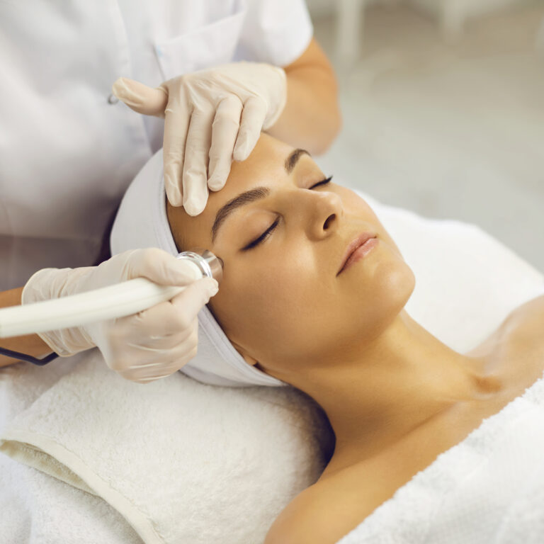 Cosmetologist making vacuum facial skin cleaning for young woman in beauty salon